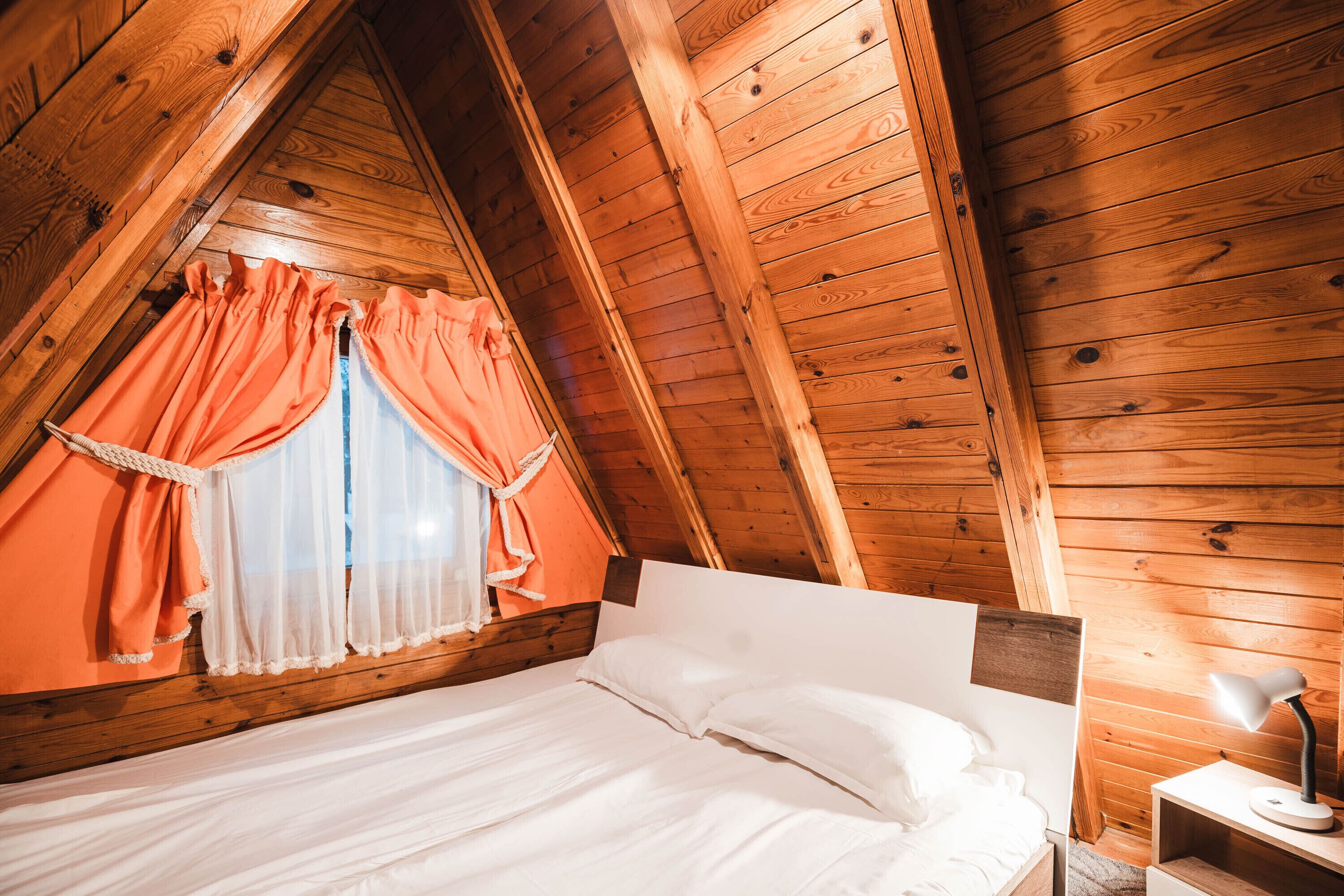 Habitación con paneles de madera, una cama, una mesita de noche y una ventana con cortinas naranjas.