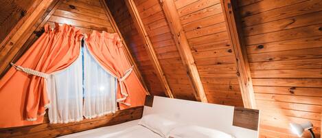 Een kamer met houten lambrisering, een bed, nachtkastje en een raam met oranje gordijnen.