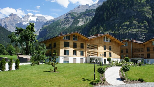 A wooden chalet with multiple balconies, surrounded by a well-maintained lawn and a pathway leading to the entrance. - Victoria Alpine Park (Kandersteg)