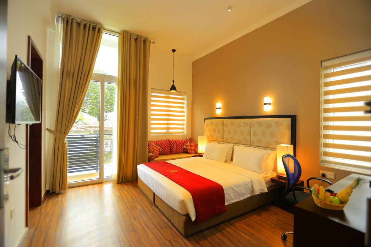 A hotel room with a large bed, a desk with a chair, a television, and a window with blinds.