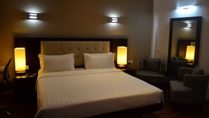 A hotel room with a large bed, two bedside lamps, a headboard, a round table, and a chair. - Ripon Grand Hill (Nuwara Eliya)