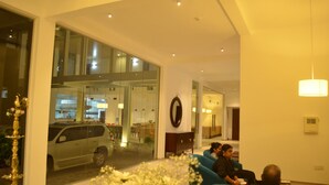 A modern hotel lobby with a large glass wall, seating area, and a visible kitchen in the background. - Ripon Grand Hill (Nuwara Eliya)