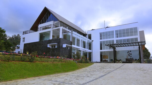 A modern two-story building with a glass facade, a stone base, and a landscaped garden with colorful flowers. - Ripon Grand Hill (Nuwara Eliya)