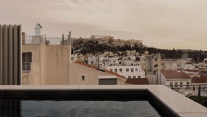 A rooftop pool with a view of a historic cityscape, including ancient ruins on a hill. - Perianth Hotel, a member of Design Hotels (Athens)