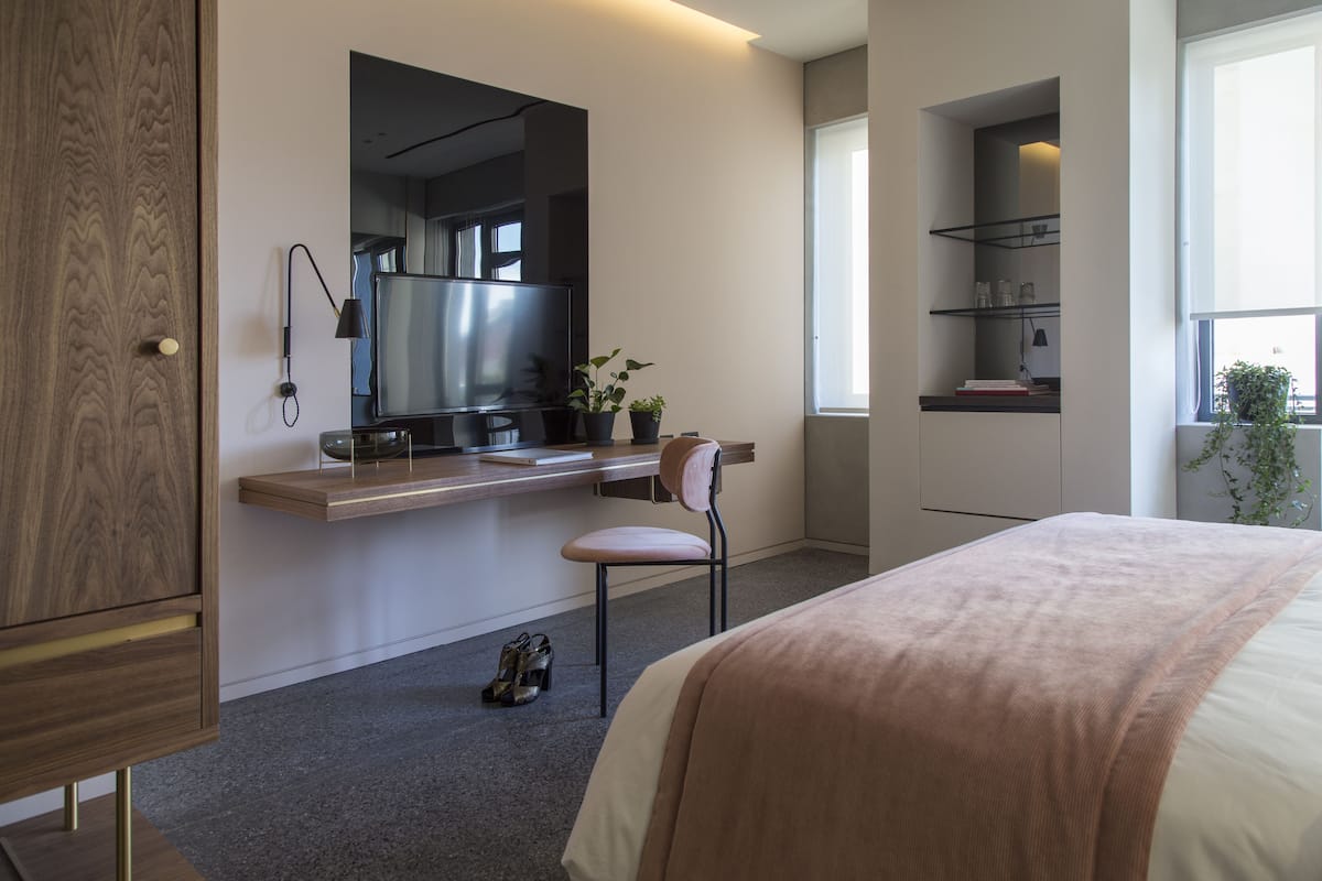 A modern hotel room with a large bed, a desk with a computer, a TV, and a window with a view.