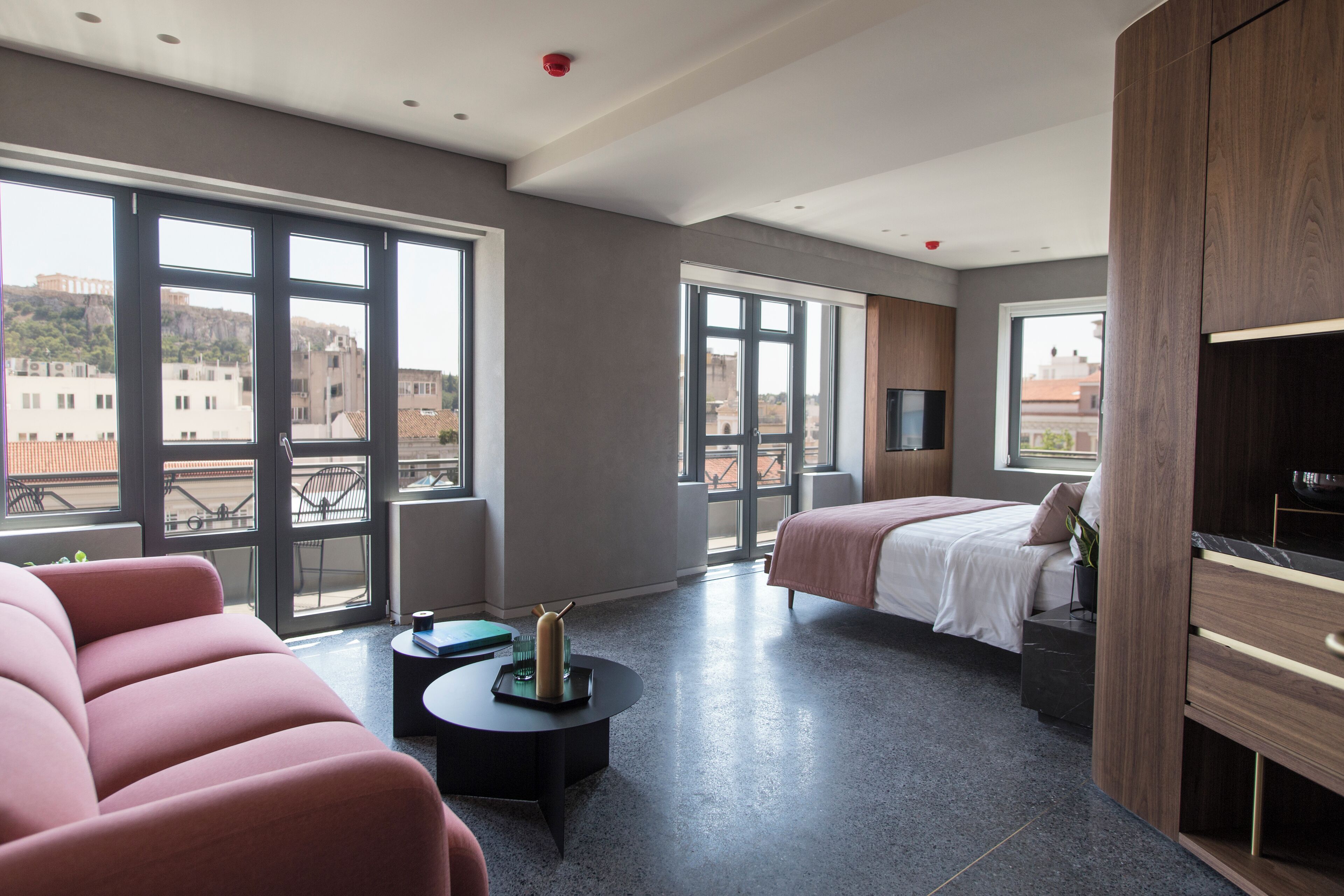 Quarto de hotel moderno com uma cama grande, um sofá, uma TV e vista para a cidade.