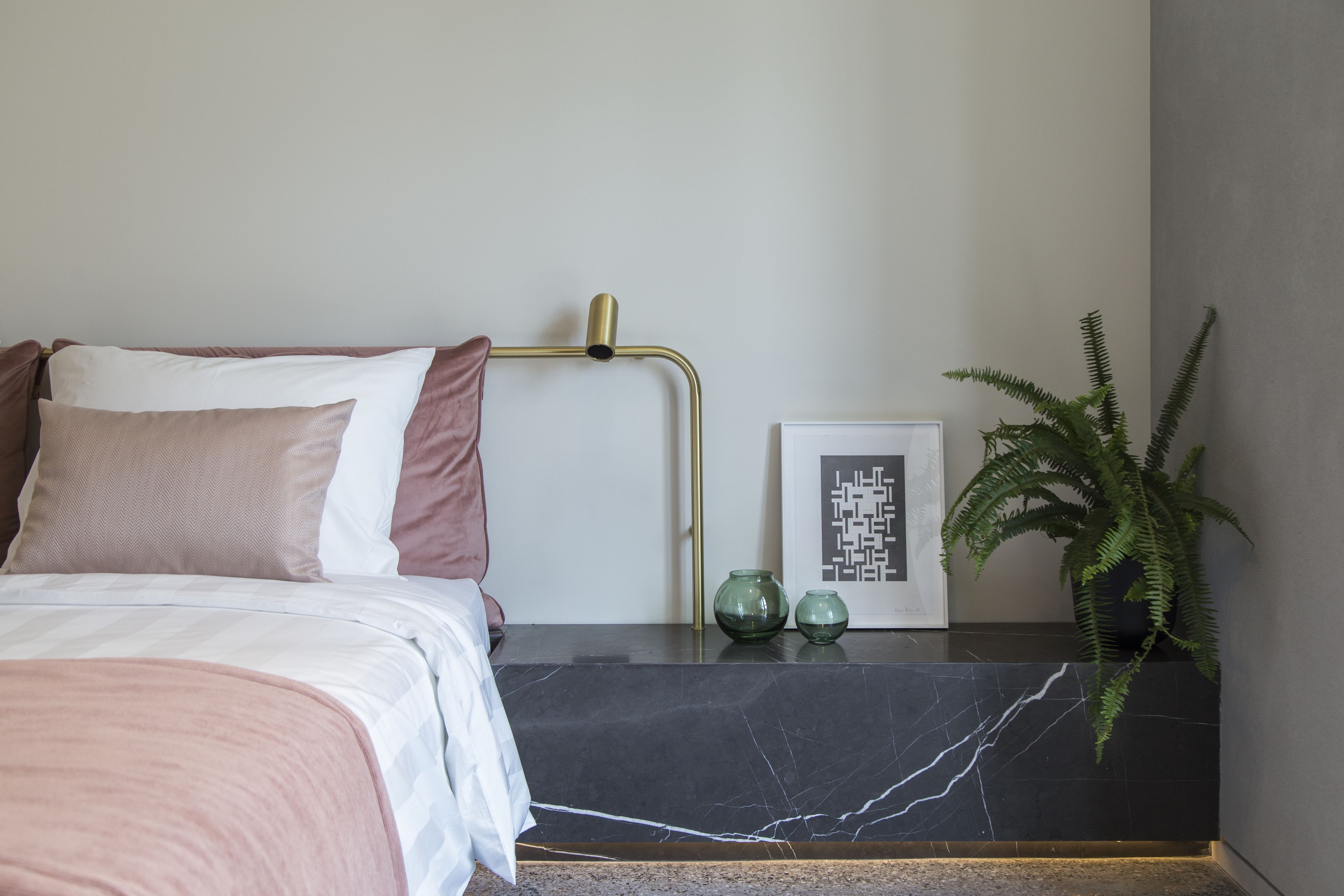 A neatly arranged bedroom with a bed, bedside table, and a potted plant.