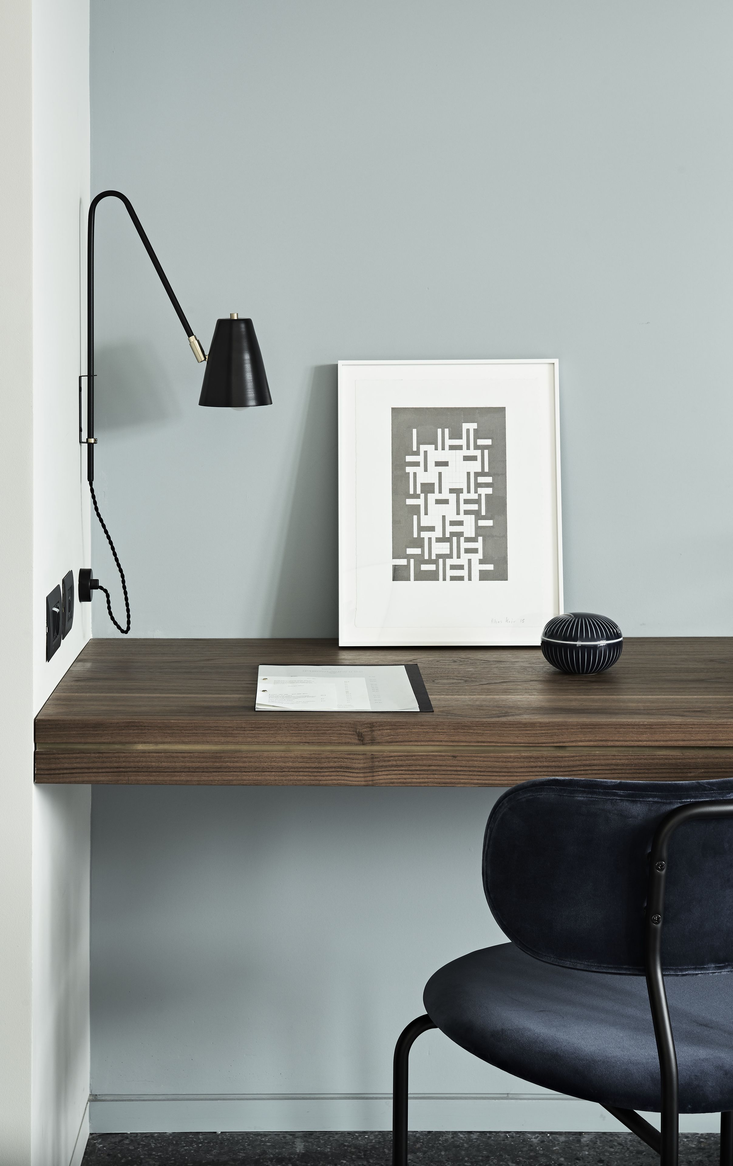 Un bureau moderne avec une lampe noire, une œuvre d’art abstraite encadrée et une chaise noire.