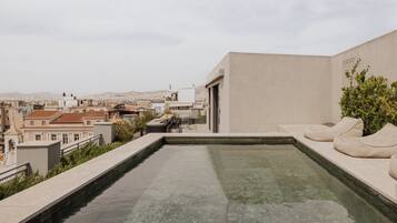 A rooftop pool with a seating area, surrounded by buildings and a view of the cityscape.