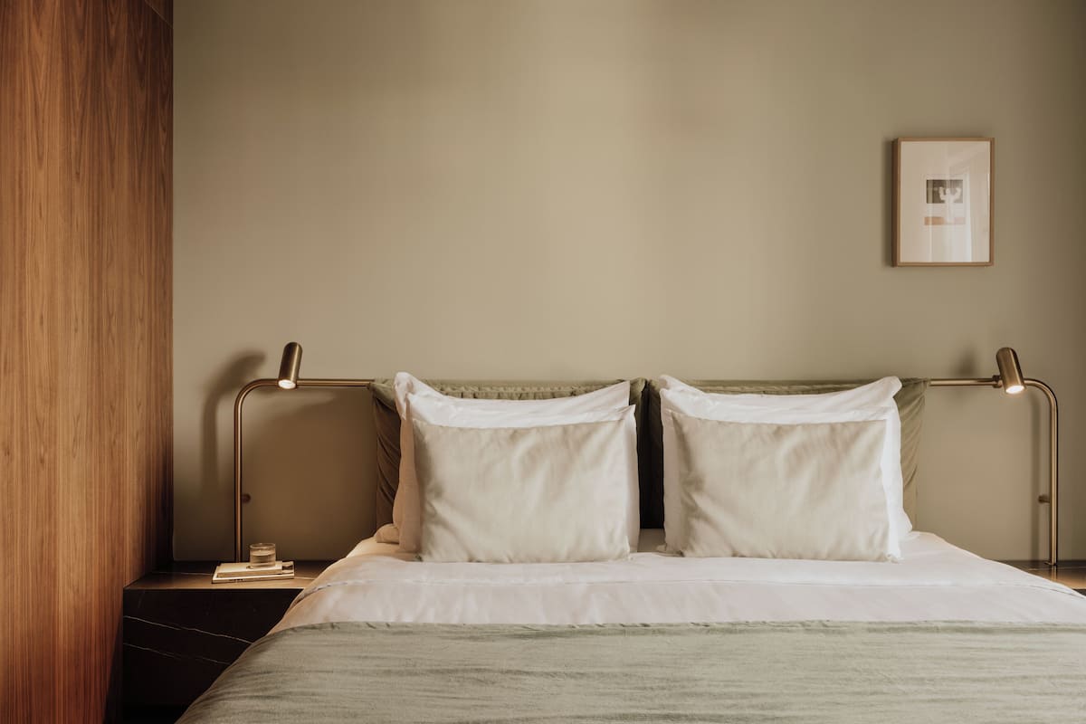 A neatly made bed with white linens, a bedside table with a book, and a framed picture on the wall.