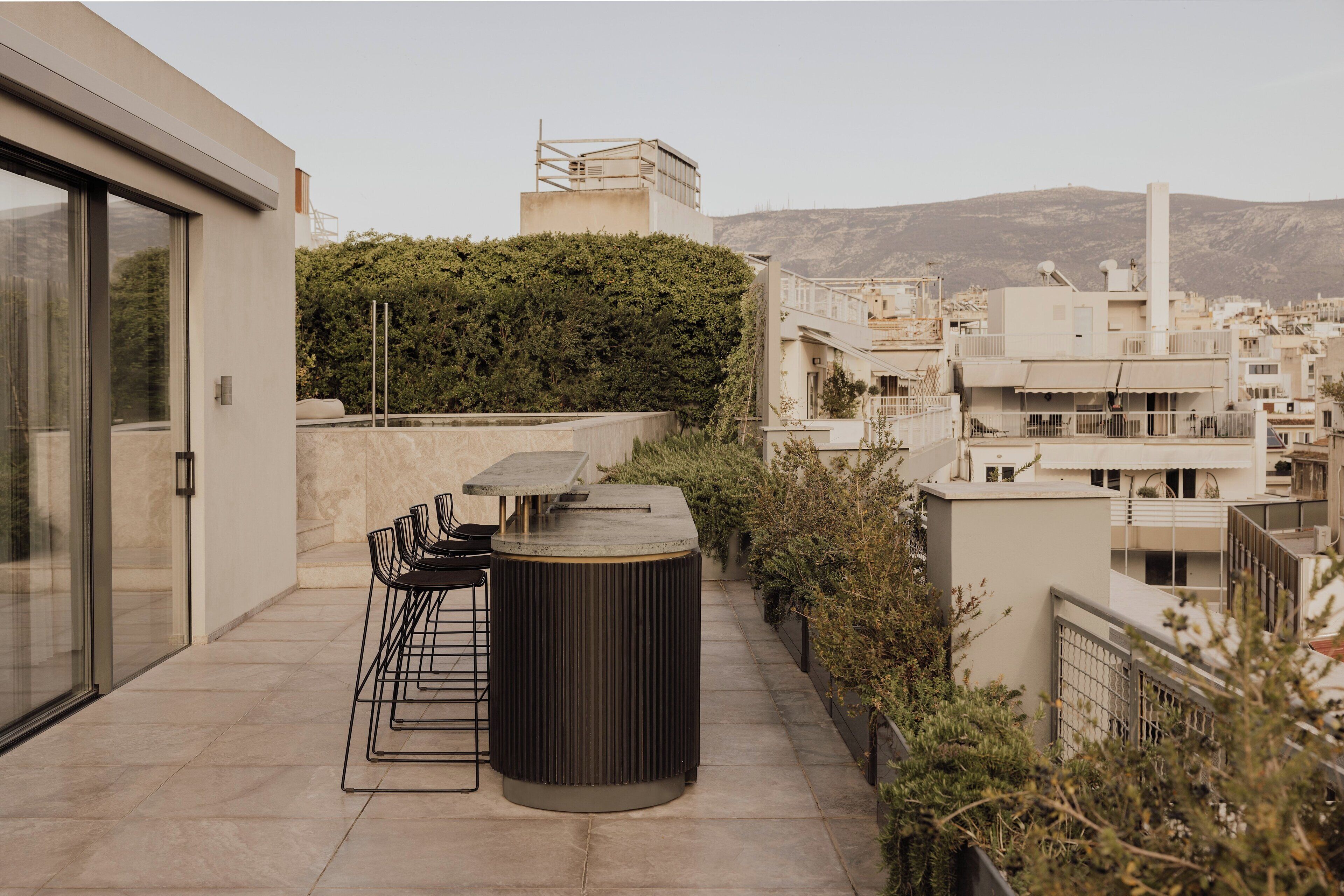 A rooftop terrace with a table and chairs, a trash bin, and a view of the city and hills in the background.