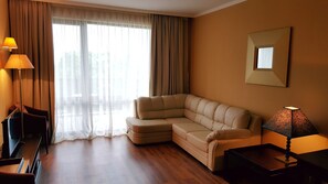 A modern living room with a sectional sofa, a flat-screen TV, and a lamp. - Sandapart Royal Beach Apartments (Sunny Beach)