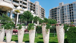 Un hotel con varios balcones, un jardín bien cuidado lleno de flores y un cielo azul despejado.