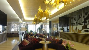 Un vestíbulo espacioso con un sofá curvo de color oscuro, una mesa redonda dorada y un candelabro decorativo dorado.