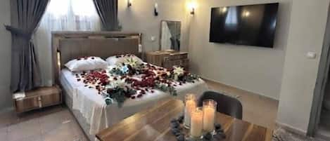 A hotel room with a bed, a dining table with candles, a TV mounted on the wall, and an air conditioning unit.