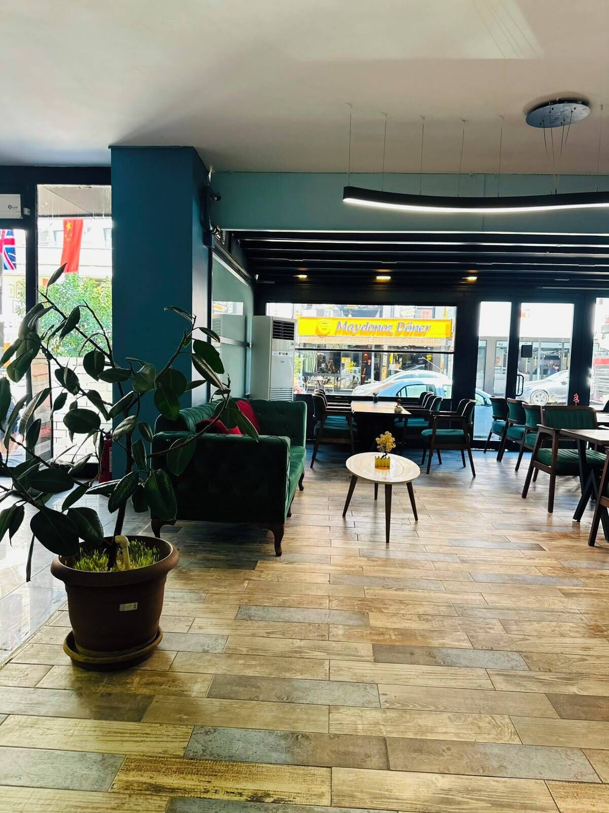 Ruime binnenruimte met een groene bank, een ronde tafel met een vaas, en een potplant.