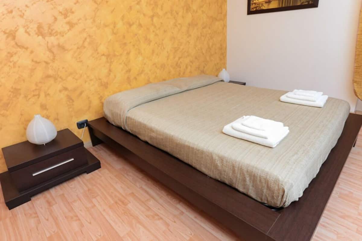 Un lit bien fait, recouvert d’une couverture beige, avec deux serviettes blanches pliées posées sur le bord.