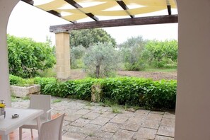 An outdoor patio with stone flooring, a table with chairs, and a pergola overhead. - Agriturismo Capani (Alezio)
