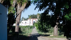 A pathway leading to a building with a red and white facade, surrounded by trees and greenery. - Agriturismo Capani (Alezio)