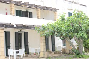 A building with a terrace, outdoor seating, and a tree. - Agriturismo Capani (Alezio)
