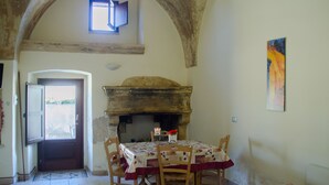A dining area with a table set for four, a fireplace, and a window with an open door. - Agriturismo Capani (Alezio)