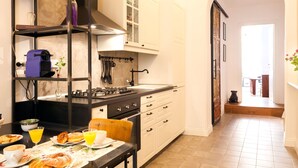A modern kitchen with white cabinets, a black countertop, and a dining area with breakfast items. - Banco19B&B (Rome)