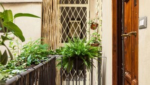 A narrow balcony with a wooden railing, a bamboo fence, and various potted plants. - Banco19B&B (Rome)