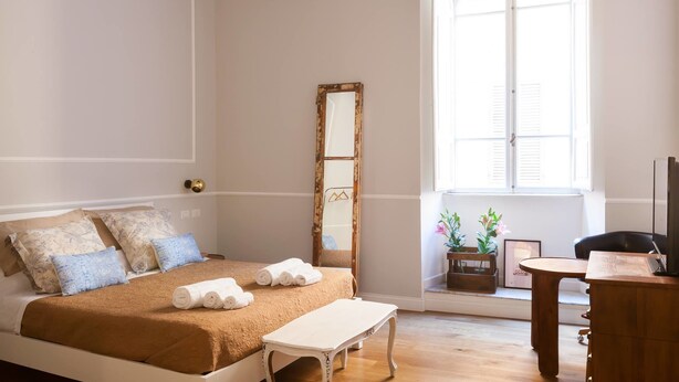 A bedroom with a bed, a bedside table, a mirror, a window with shutters, and a desk with a chair. - Banco19B&B (Rome)