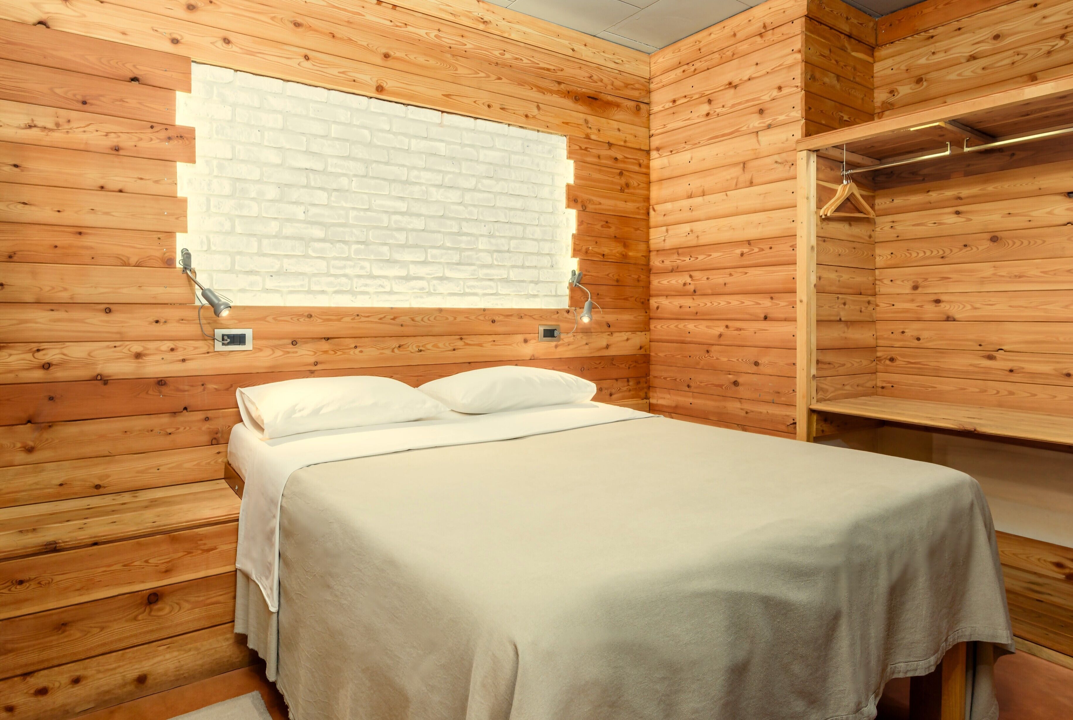 Een kamer met houten lambrisering, een bed, een kledingrek en een raam met een wit baksteenmotief.