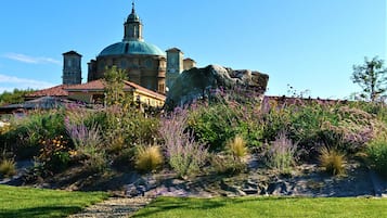 Un edificio histórico con una cúpula destacada y torres de campanas, rodeado de un jardín ajardinado con diversos arbustos y flores.