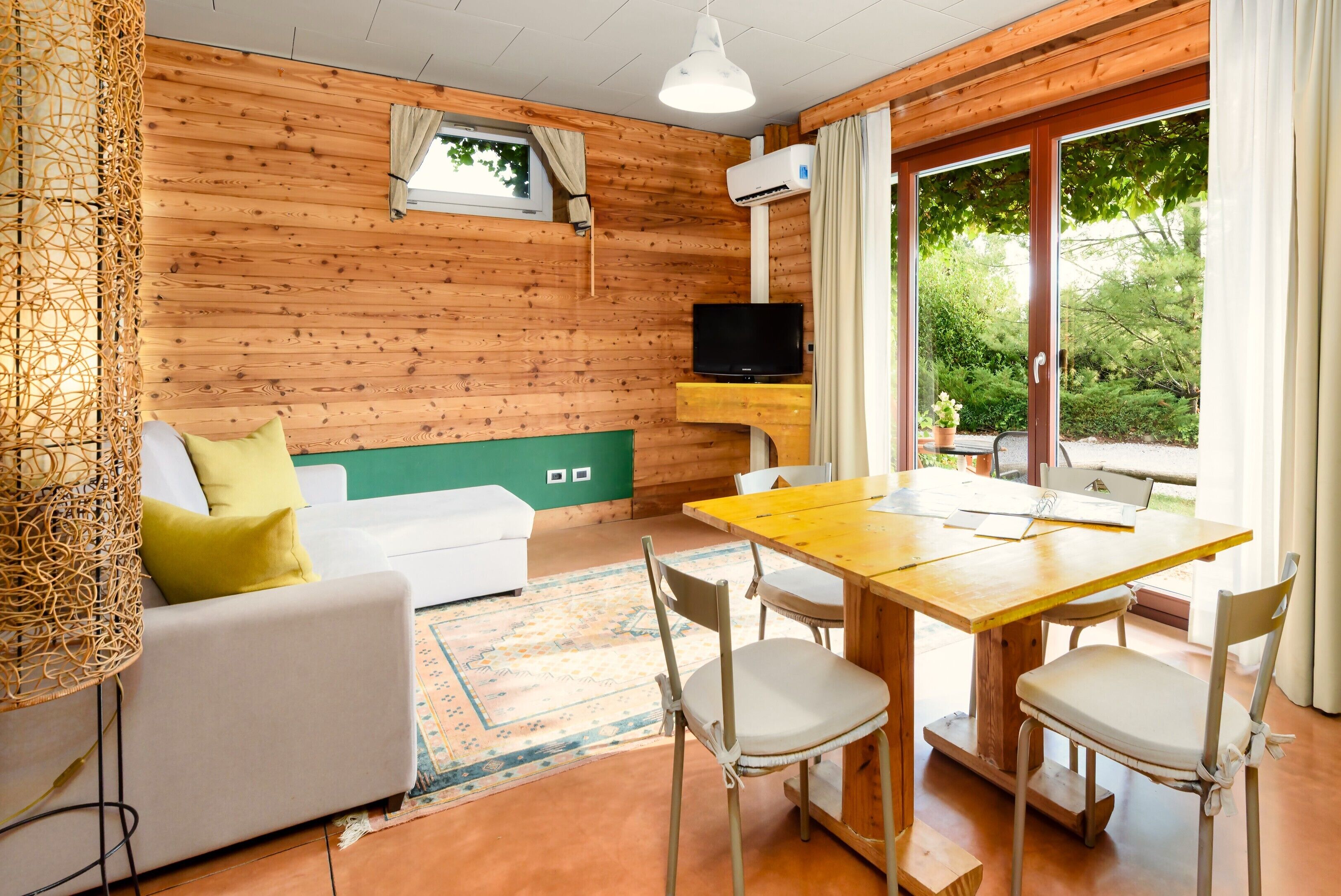 Un'accogliente stanza con arredamento in legno, un divano con cuscini, un tavolo da pranzo con sedie, una televisione e una finestra con tende.