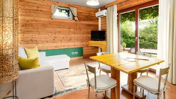 Un'accogliente stanza con arredamento in legno, un divano con cuscini, un tavolo da pranzo con sedie, una televisione e una finestra con tende.