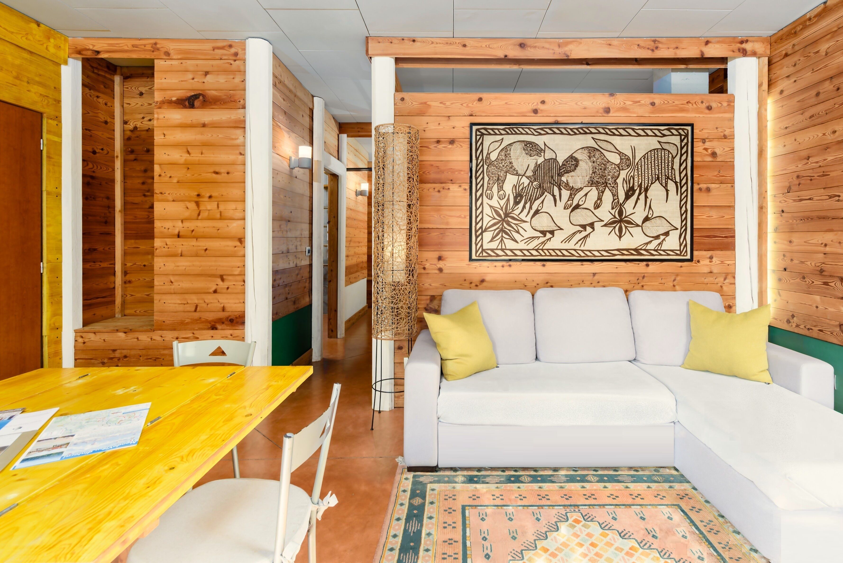 A room with a wooden interior, a white sofa, a yellow table, and a patterned rug.