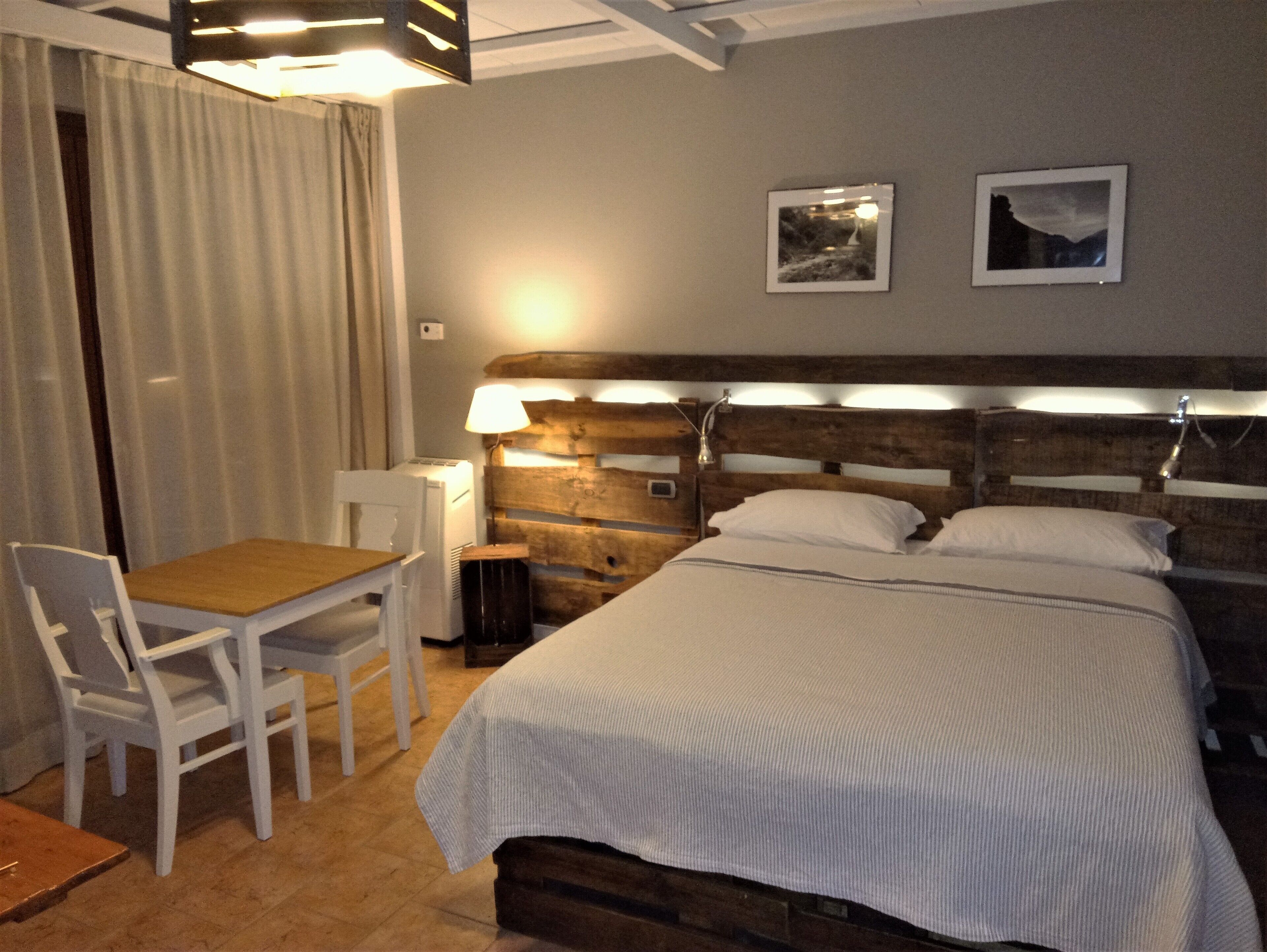 Ein Hotelzimmer mit hölzernem Kopfteil, einem Einzelbett, einem kleinen Tisch mit Stuhl und zwei gerahmten Bildern an der Wand.