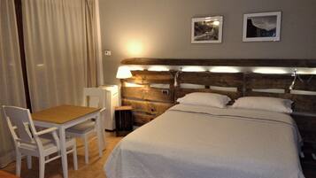 Ein Hotelzimmer mit hölzernem Kopfteil, einem Einzelbett, einem kleinen Tisch mit Stuhl und zwei gerahmten Bildern an der Wand.