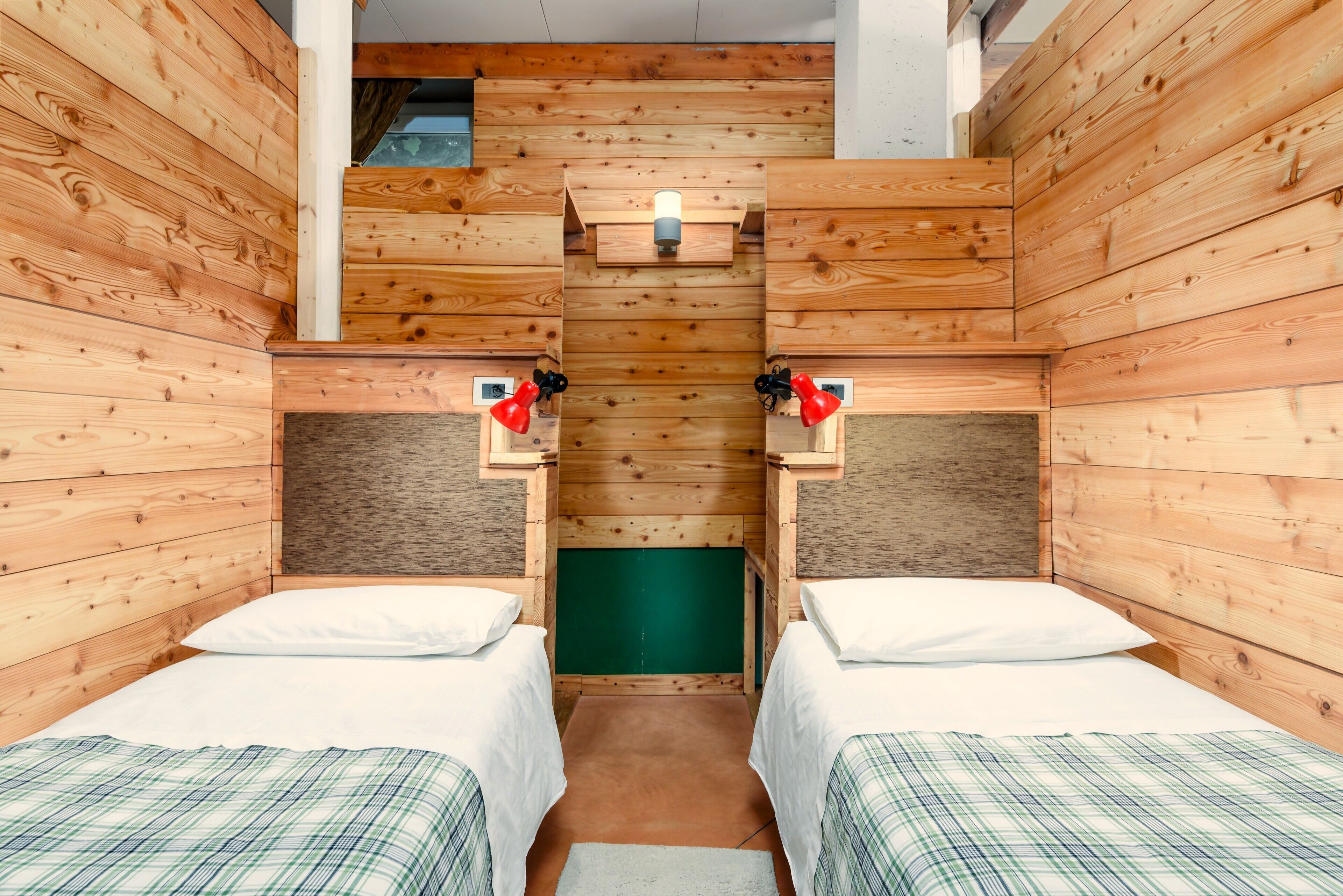 Une pièce en bois avec deux lits, un mur vert et une petite fenêtre.