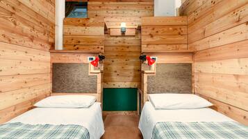Une pièce en bois avec deux lits, un mur vert et une petite fenêtre.