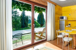 Una habitación con puerta corrediza de vidrio que da a un jardín, una mesa de madera con sillas, un refrigerador pequeño y un microondas sobre una pared amarilla.
