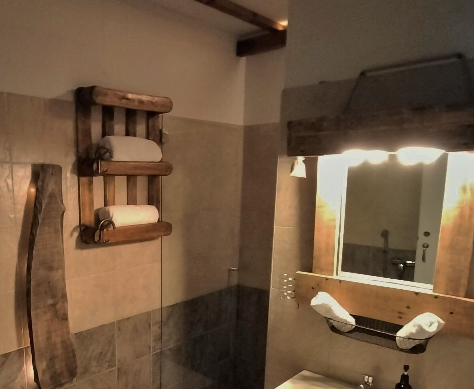 Ein Badezimmer mit einem hölzernen Regal mit Handtüchern, einem Spiegel mit Beleuchtung darüber und einem Waschbecken mit Handtuchhalter.
