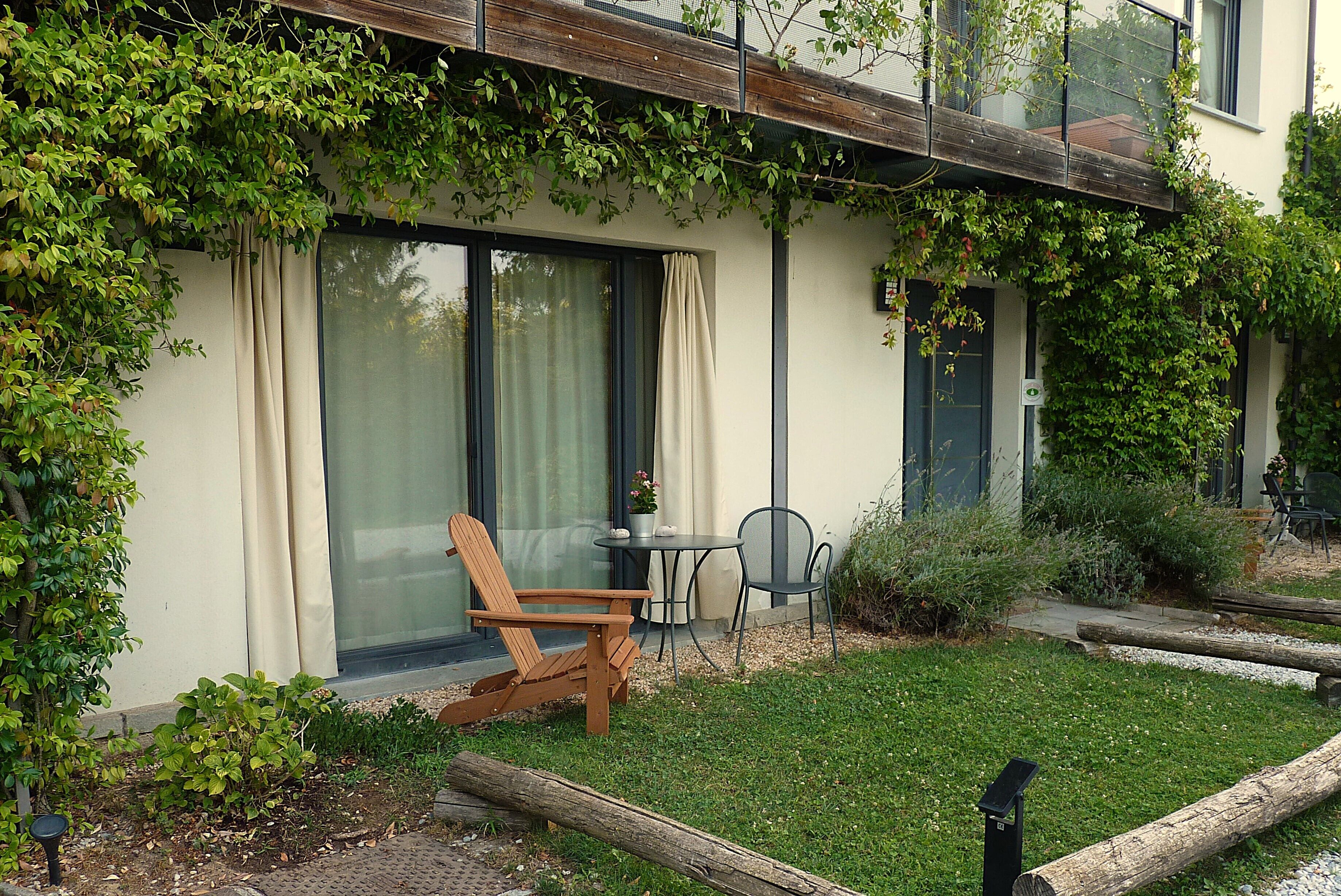 Una casa moderna con jardín, una silla de madera, una mesa y una planta en maceta.