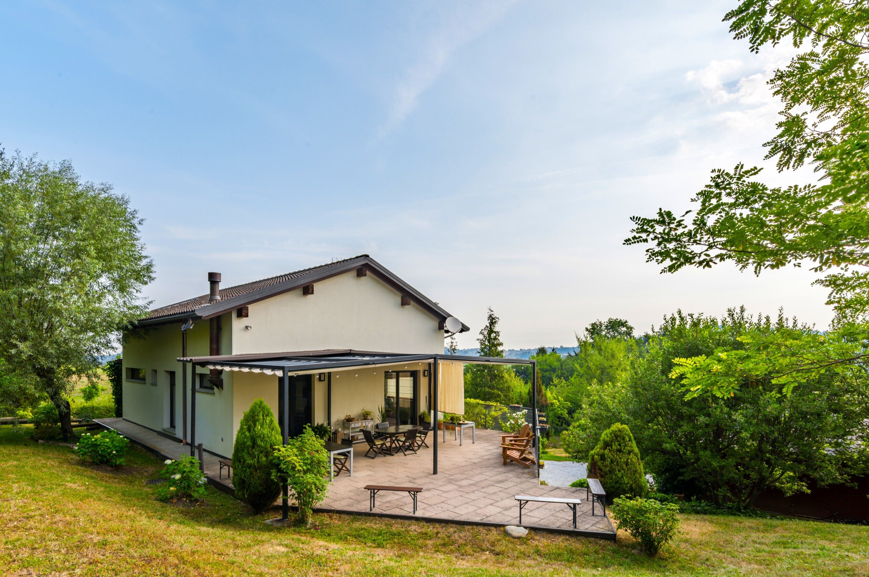 Ein Haus mit überdachter Terrasse, einem Rasen und Blick auf die grüne Umgebung.