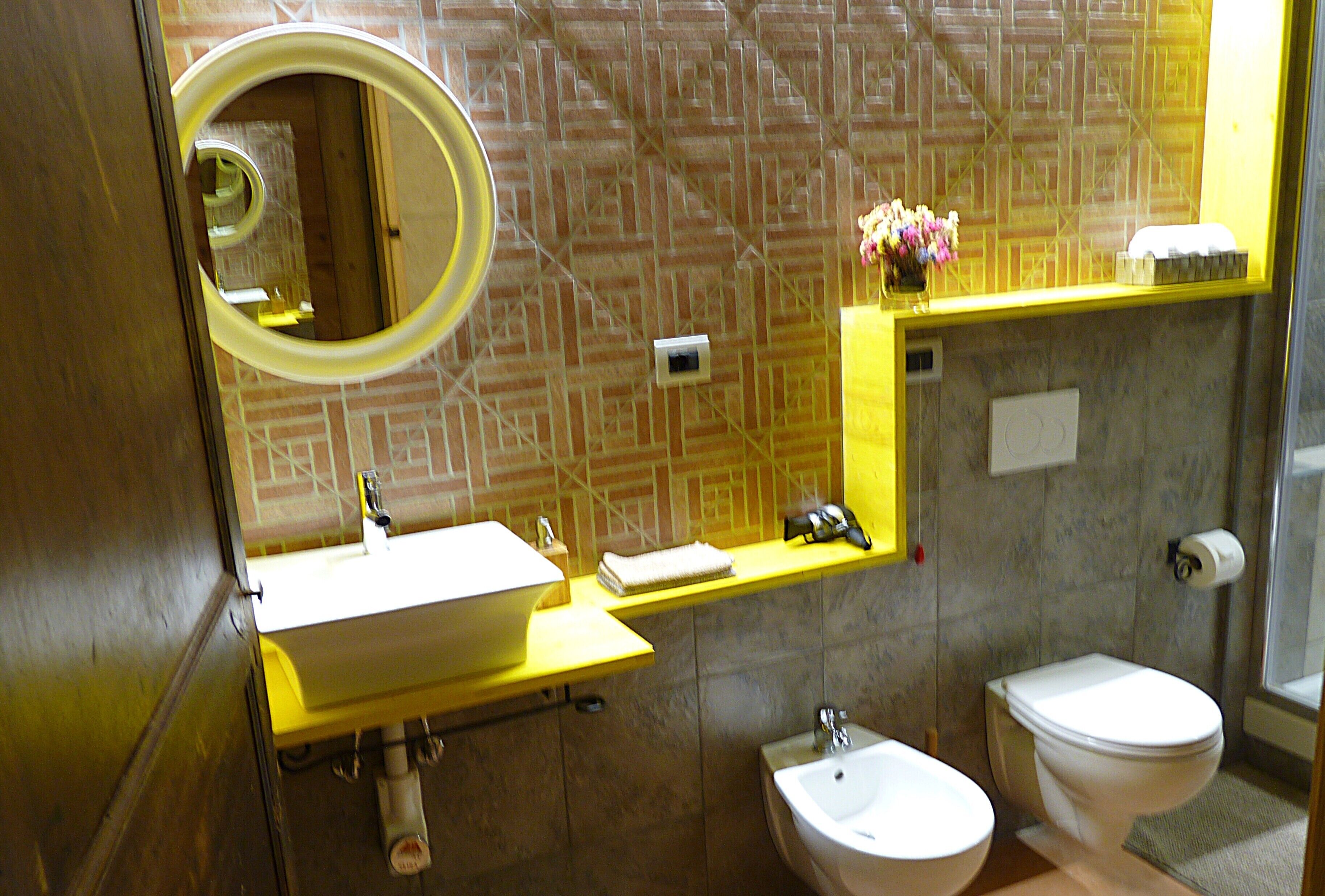 Une salle de bain équipée d’un lavabo, d’un miroir, de toilettes et d’une petite étagère sur laquelle se trouve un vase.