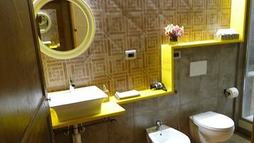 Une salle de bain équipée d’un lavabo, d’un miroir, de toilettes et d’une petite étagère sur laquelle se trouve un vase.