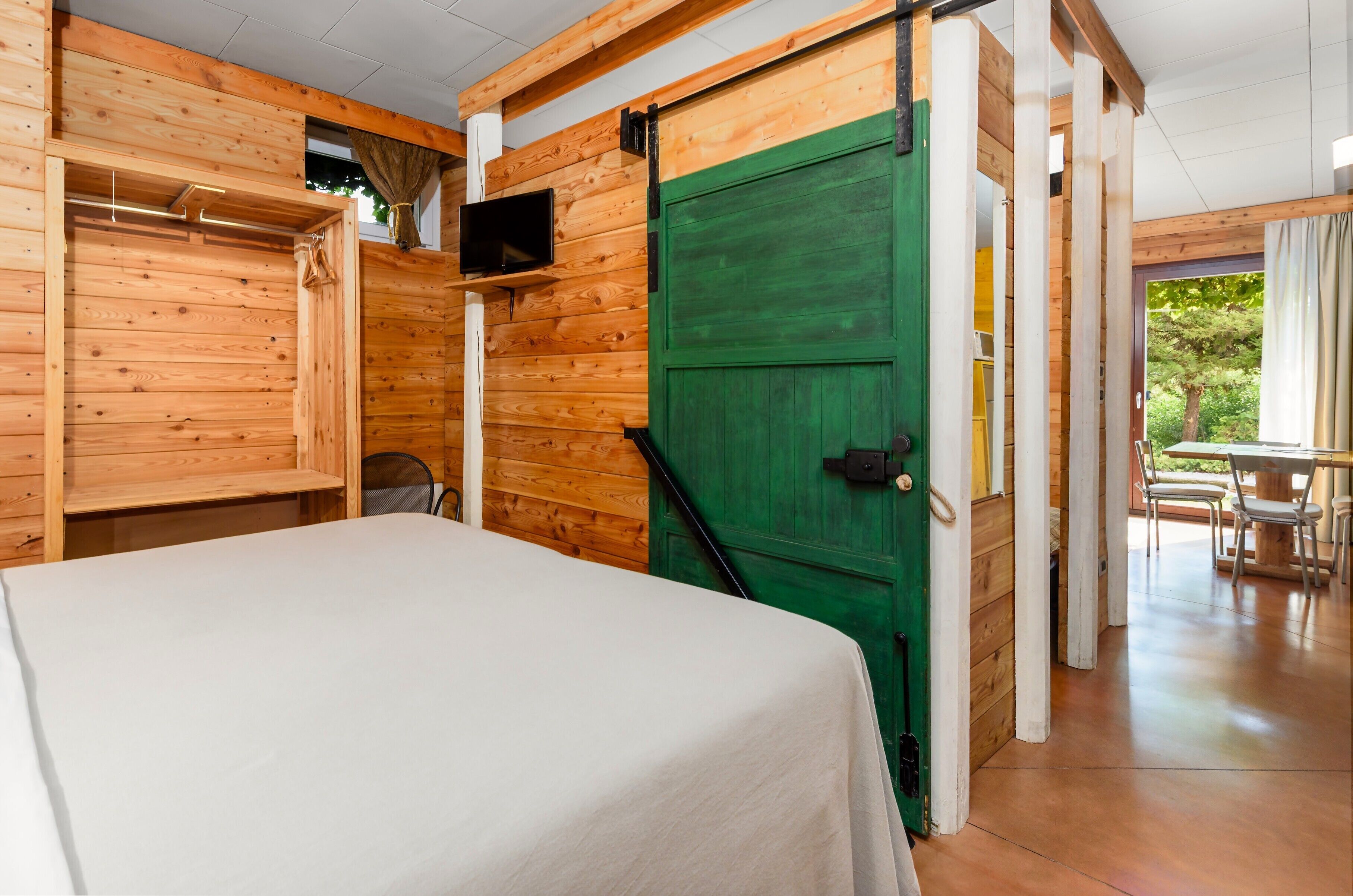 A room with a bed, a green door, and a view of the outdoors.