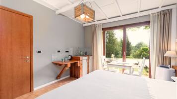 Quarto com cama, escrivaninha de madeira, janela com cortinas e vista para o verde lá fora.