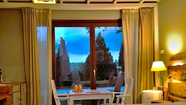 Habitación de hotel con cama, una mesa y sillas, una lámpara y vista a un templo a través de una ventana.