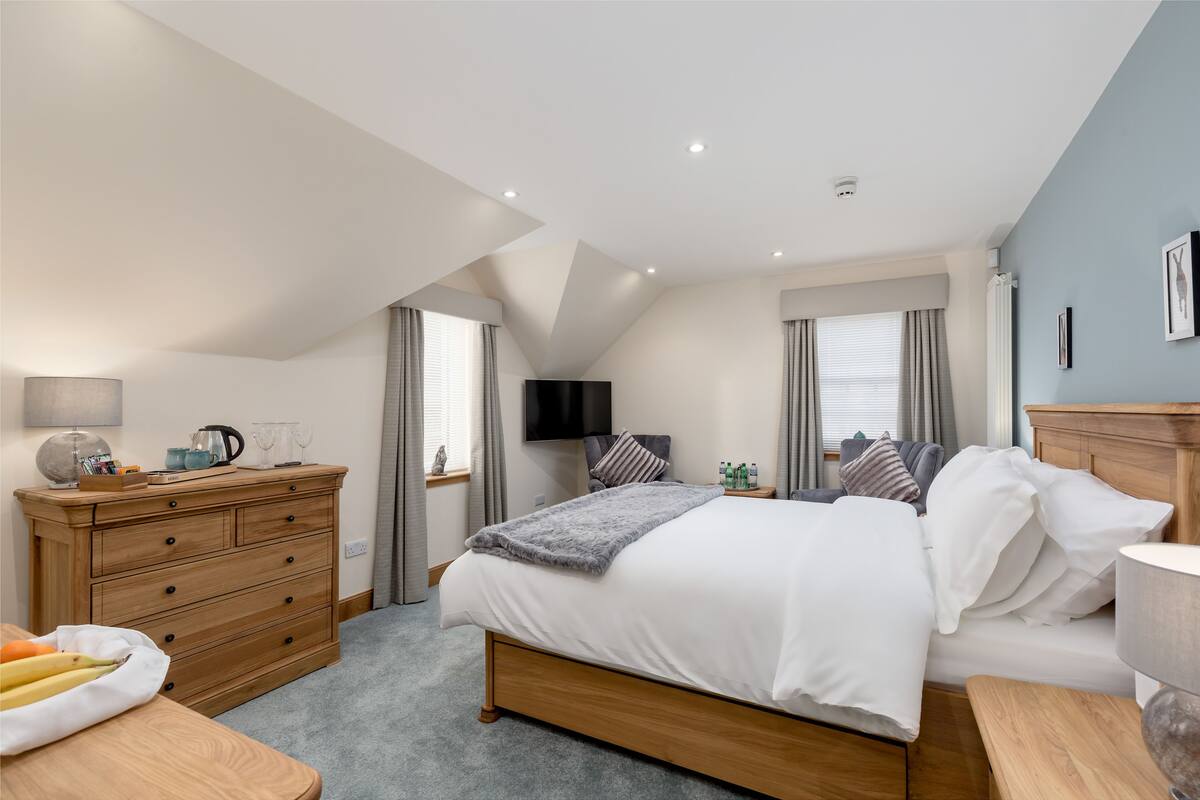A bedroom with a bed, dresser, TV, and windows.