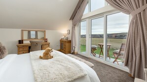 A bedroom with a large bed, a desk, a chair, and a view of a grassy field through large windows. - The Queens View Luxury B&B (Linlithgow)