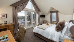 A bedroom with a large bed, a desk, a chair, and a view of the outdoors through a sliding glass door. - The Queens View Luxury B&B (Linlithgow)