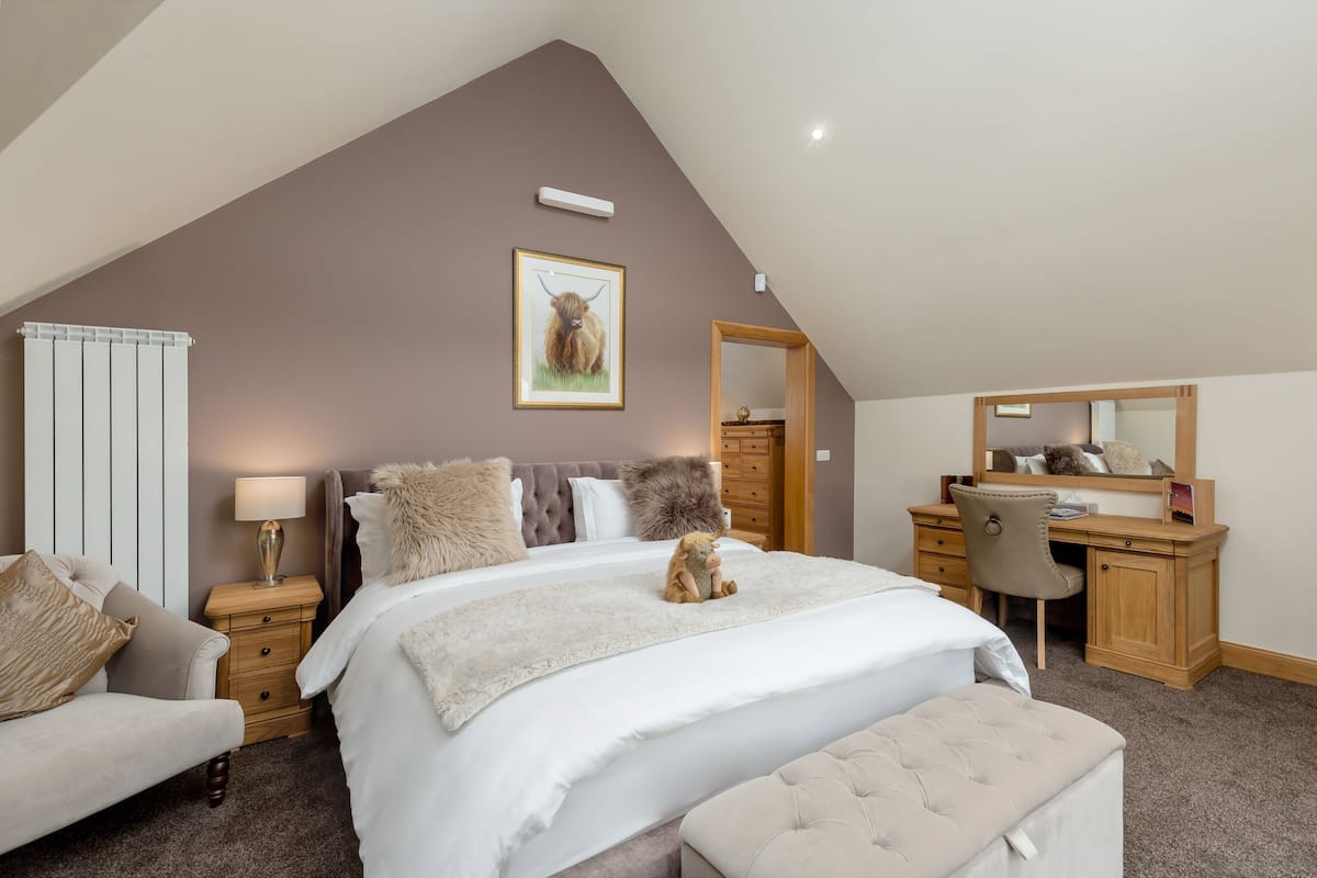 A bedroom with a large bed, a desk, and a chair. There is a radiator, a lamp, and a framed picture on the wall.